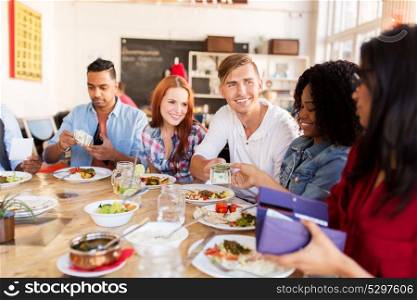 leisure, payment and people concept - happy friends with money paying for food at restaurant. happy friends with money paying at restaurant