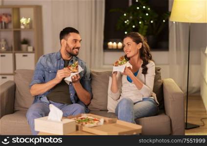 leisure, people and fast food concept - happy couple eating takeaway pizza at home in evening. happy couple eating takeaway pizza at home