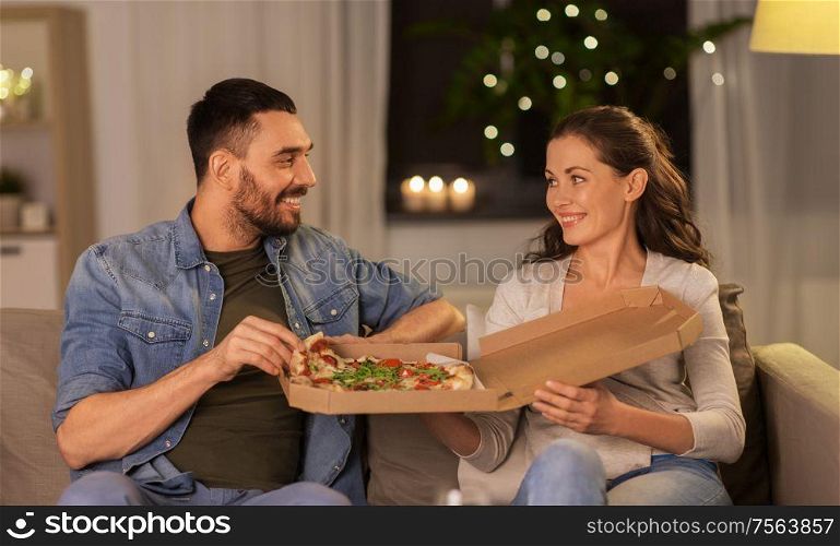 leisure, people and fast food concept - happy couple eating takeaway pizza at home in evening. happy couple eating takeaway pizza at home