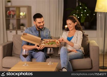 leisure, people and fast food concept - happy couple with wine eating takeaway pizza at home in evening. happy couple eating takeaway pizza at home