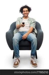 leisure, people and furniture concept - happy smiling young man in glasses tv remote control sitting in chair over white background. happy man with tv remote control sitting in chair
