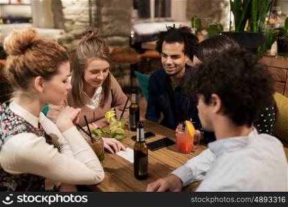 leisure, people and holidays concept - happy friends with drinks and bill at bar or cafe
