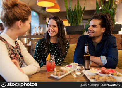 leisure, people and holidays concept - happy friends with drinks and food at bar or cafe. happy friends with drinks and food at bar or cafe