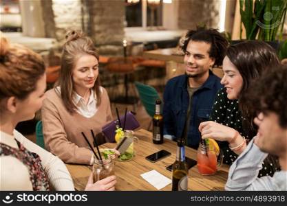 leisure, people and holidays concept - happy friends with drinks, credit card and bill at bar or cafe