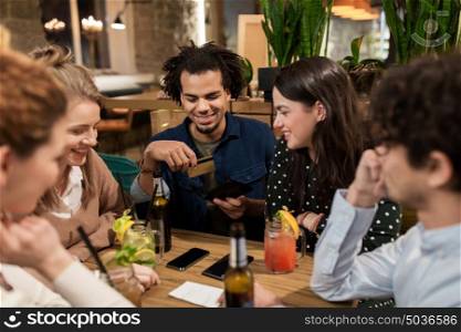 leisure, people and holidays concept - happy friends with drinks, credit card and bill at bar or cafe. friends with drinks, credit card and bill at bar