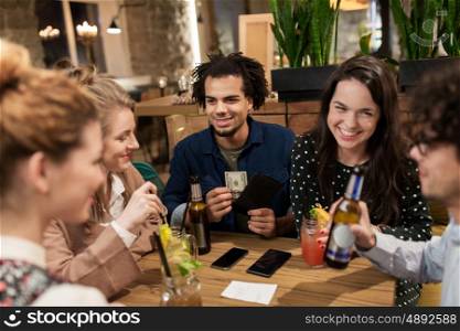 leisure, people and holidays concept - happy friends with drinks, money and bill at bar or cafe