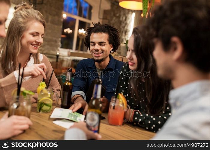 leisure, people and holidays concept - happy friends with drinks, money and bill at bar or cafe. friends with drinks, money and bill at bar