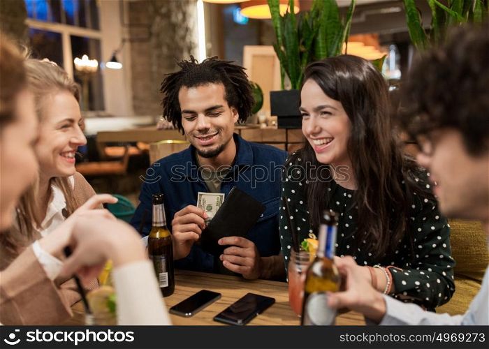 leisure, people and holidays concept - happy friends with drinks, money and smartphones at bar or cafe. friends with drinks, money and bill at bar