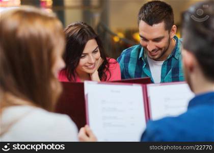 leisure, people and holidays concept - smiling couple with friends reading menu at restaurant
