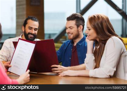 leisure, people and holidays concept - smiling friends discussing menu at restaurant