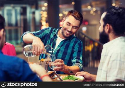 leisure, people and holidays concept - smiling man with friends pouring water from jug at restaurant. happy man with friends pouring water at restaurant. happy man with friends pouring water at restaurant