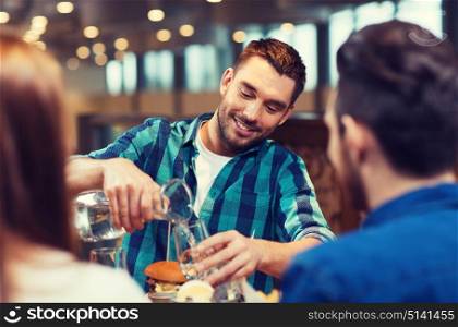 leisure, people and holidays concept - smiling man with friends pouring water from jug at restaurant. happy man with friends pouring water at restaurant