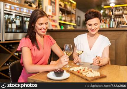 leisure, people and lifestyle concept - happy women eating snacks at wine bar or restaurant. women eating snacks at wine bar or restaurant