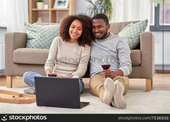 leisure, people and technology concept - happy african american couple with laptop computer and takeaway pizza and drinking red wine at home. happy couple with laptop drinking red wine at home