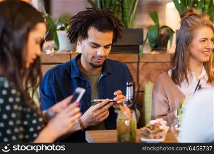leisure, people and technology concept - happy friends with smartphones eating and drinking at restaurant. friends with smartphones eating at restaurant
