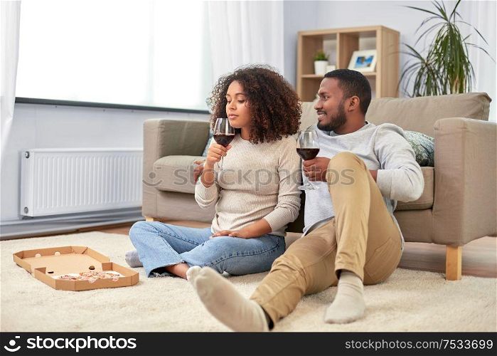 leisure, people and valentines day concept - happy african american couple with wine and takeaway pizza at home. happy couple with wine and takeaway pizza at home