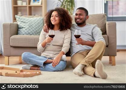 leisure, people and valentines day concept - happy african american couple with wine and takeaway pizza at home. happy couple with wine and takeaway pizza at home
