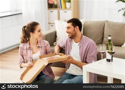 leisure, people and valentines day concept - happy couple with wine eating takeaway pizza at home. couple with wine eating takeaway pizza at home