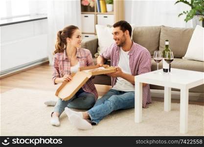 leisure, people and valentines day concept - happy couple with wine eating takeaway pizza at home. couple with wine eating takeaway pizza at home