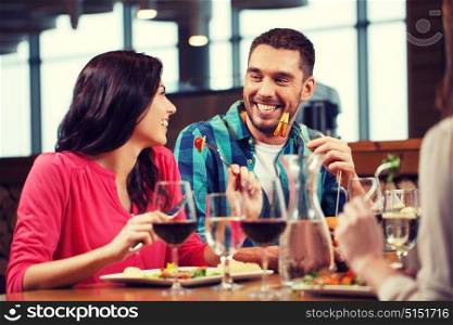 leisure, people, eating and holidays concept - happy couple with friends having dinner at restaurant. happy couple with friends eating at restaurant