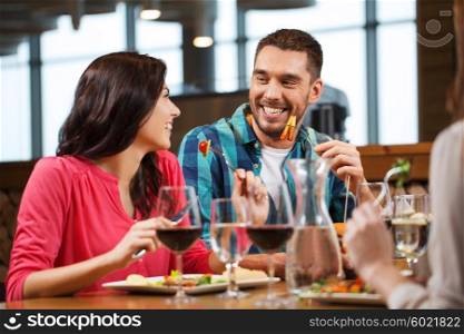 leisure, people, eating and holidays concept - happy couple with friends having dinner at restaurant