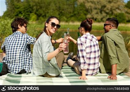 leisure, picnic and people concept - friends drinking beer and cider on lake pier in summer park. friends drinking beer and cider on lake pier