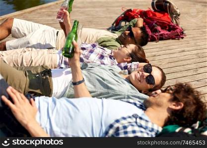 leisure, picnic and people concept - friends drinking beer and cider on lake pier in summer park. friends drinking beer and cider on lake pier