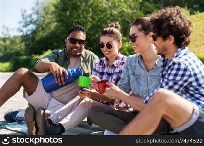 leisure, picnic and people concept - happy friends drinking tea from thermos outdoors in summer park. happy friends drinking tea from thermos in summer