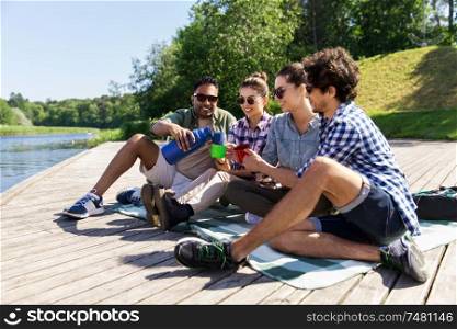 leisure, picnic and people concept - happy friends drinking tea from thermos outdoors in summer park. happy friends drinking tea from thermos in summer