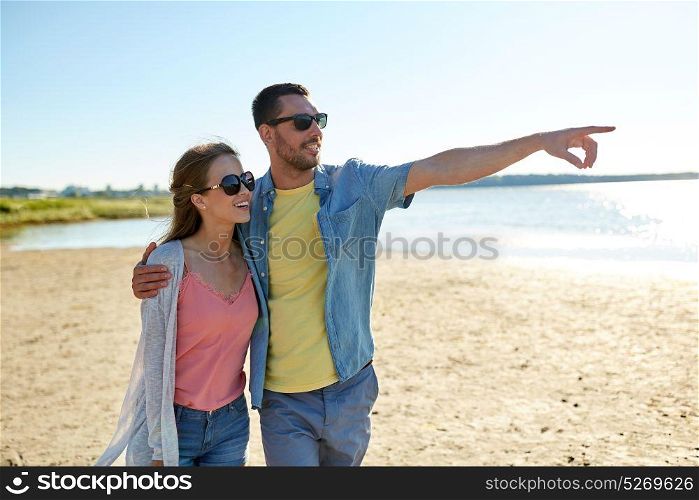 leisure, relationship and people concept - happy couple hugging on summer beach and pointing finger to something. happy couple hugging on summer beach