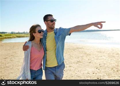 leisure, relationship and people concept - happy couple hugging on summer beach and pointing finger to something. happy couple hugging on summer beach