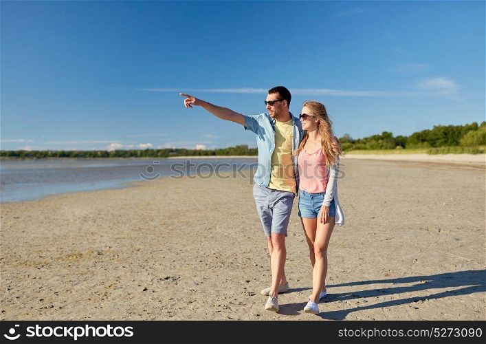 leisure, relationship and people concept - happy couple walking along summer beach and pointing finger to something. happy couple walking along summer beach