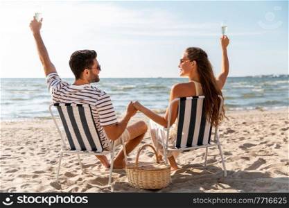 leisure, relationships and people concept - happy couple drinking ch&agne sitting in folding chairs on summer beach. happy couple drinking ch&agne on summer beach