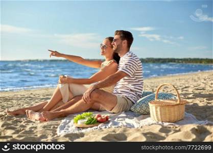 leisure, relationships and people concept - happy couple in sunglasses having picnic on summer beach. happy couple having picnic on summer beach