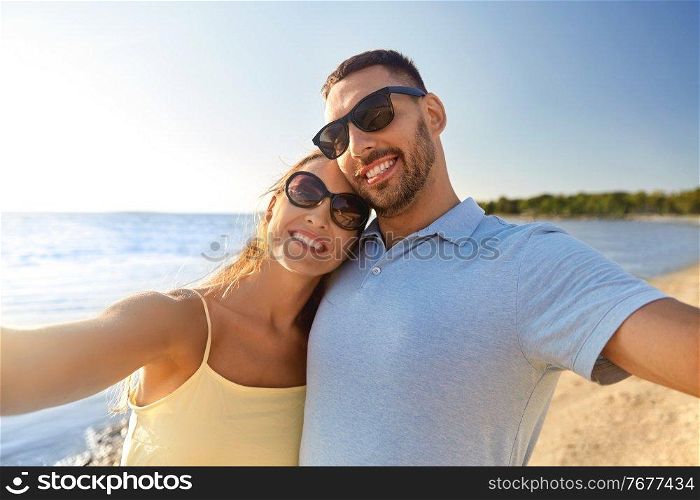 leisure, relationships and people concept - happy couple in sunglasses hugging and taking selfie on summer beach. happy couple taking selfie on summer beach