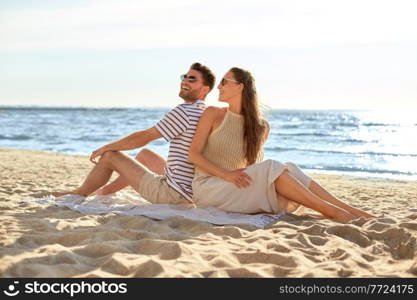 leisure, relationships and people concept - happy couple in sunglasses sitting back to back on summer beach. happy couple sitting back to back on summer beach