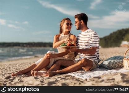 leisure, relationships and people concept - happy couple with food eating and having picnic on beach. happy couple with food having picnic on beach