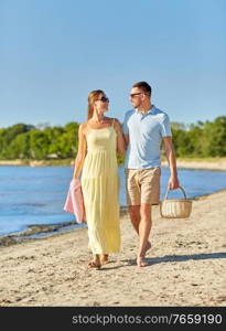 leisure, relationships and people concept - happy couple with picnic basket walking along beach. happy couple with picnic basket walking on beach