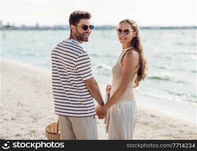 leisure, relationships and people concept - happy couple with picnic basket walking along beach. happy couple with picnic basket walking on beach