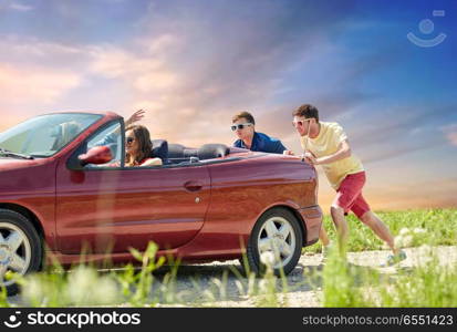 leisure, road trip, travel and people concept - friends pushing broken convertible car over sky background. friends pushing broken convertible car. friends pushing broken convertible car