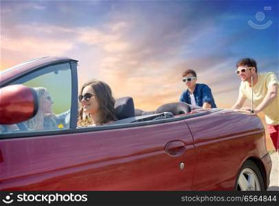 leisure, road trip, travel and people concept - friends pushing broken convertible car over sky background. friends pushing broken convertible car