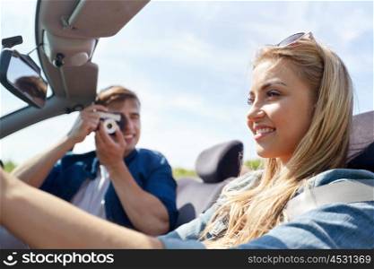leisure, road trip, travel and people concept - happy couple driving in cabriolet car and taking picture by film camera
