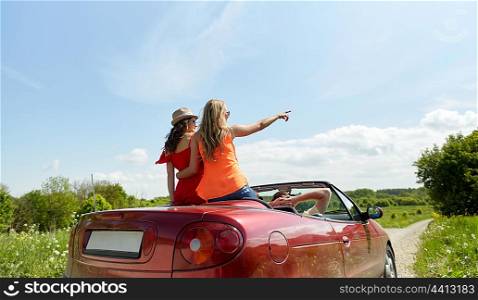 leisure, road trip, travel and people concept - happy friends driving in cabriolet car along country road and pointing finger to something