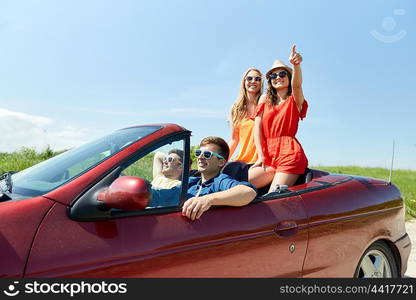 leisure, road trip, travel and people concept - happy friends driving in cabriolet car along country road and pointing finger to something