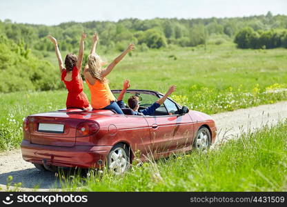 leisure, road trip, travel and people concept - happy friends driving in cabriolet car at country and waving hands