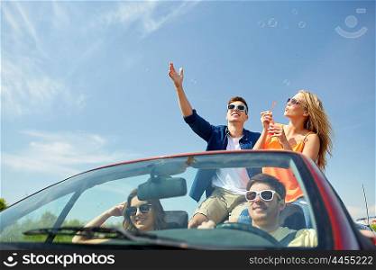 leisure, road trip, travel and people concept - happy friends driving in cabriolet car along country road and blowing bubbles