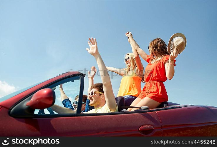 leisure, road trip, travel and people concept - happy friends driving in cabriolet car at country and waving hands
