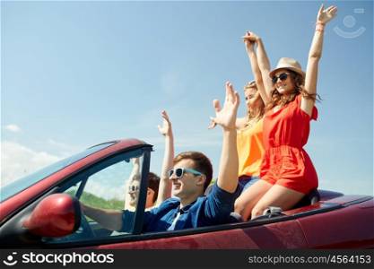 leisure, road trip, travel and people concept - happy friends driving in cabriolet car at country and waving hands