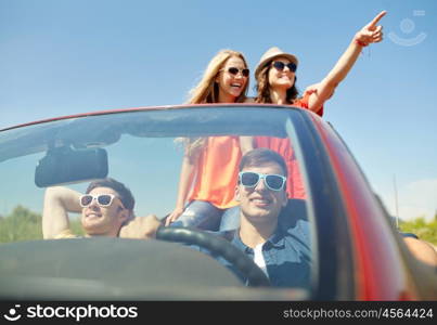 leisure, road trip, travel and people concept - happy friends driving in cabriolet car along country road and pointing finger to something