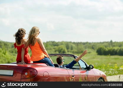 leisure, road trip, travel and people concept - happy friends driving in cabriolet car at country and waving hands